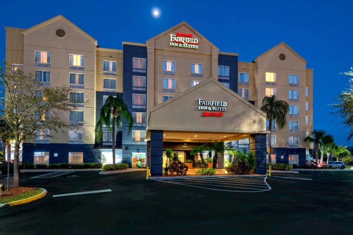 Hotel exterior at night with lit entrance and surrounding palm trees.